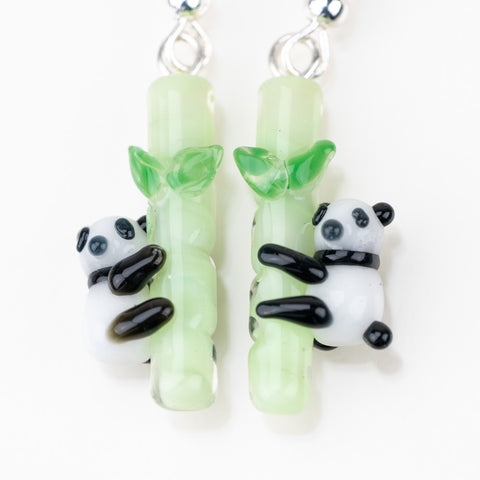 A close of up mmmelty's panda dangle earrings. Picture shows two pandas each hugging a bamboo pole.