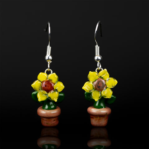 A set of sunflower themed dangle earrings on a black background. the sunflowers are composed of yellow petals, brown center, green stem, and a brown pot.