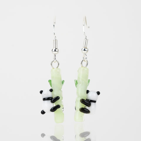 A set of two glass panda themed dangle earrings facing the back. Each earring features a black and white panda, attached to a light-green bamboo shoot. Attached to the top of the bamboo pole is a sterling silver earring hook.