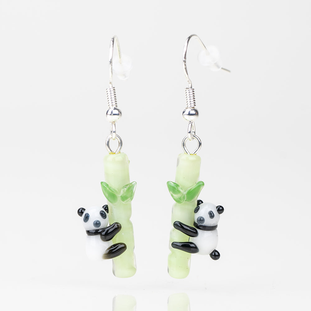 Panda themed earrings hugging a bamboo pole. The earrings are dangle style with sterling silver backing. The panda is black and white and the bamboo is UV reactive-green. 