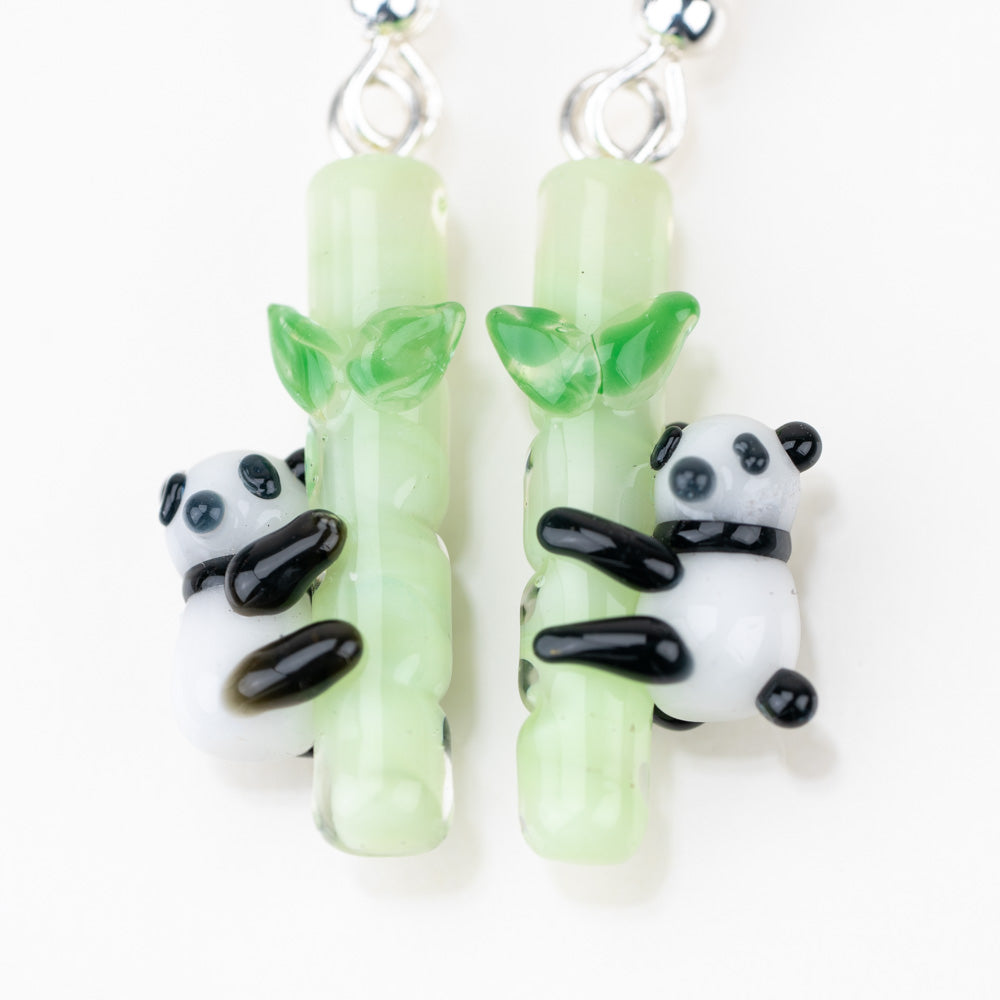 A close of up mmmelty's panda dangle earrings. Picture shows two pandas each hugging a bamboo pole. 