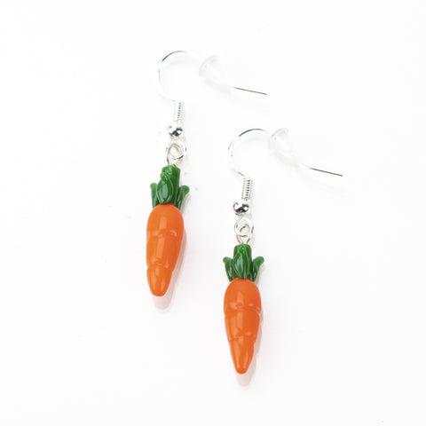 Two carrot earrings lying flat on a white table. Each earring has one carrot design with orange and green colors and a sterling silver earring hook.