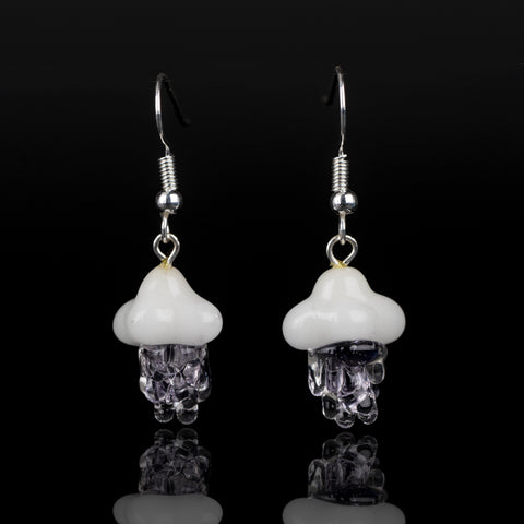 Two purple rain dangle earrings on a black background. The pieces are made entirely of glass and feature purple colored rain and a white, fluffy cloud. Attached are silver, dangle-style earrings.