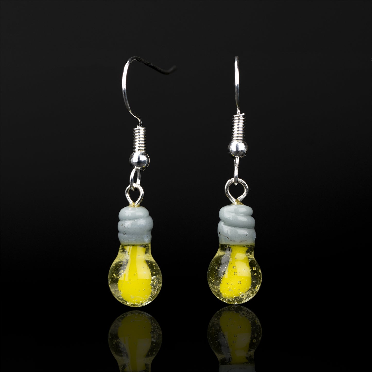 Two light bulb dangle earrings against a black background. The light bulbs havea clear and yellow bulb and grey thread. attached to the thread is a sterling silver earring hook.