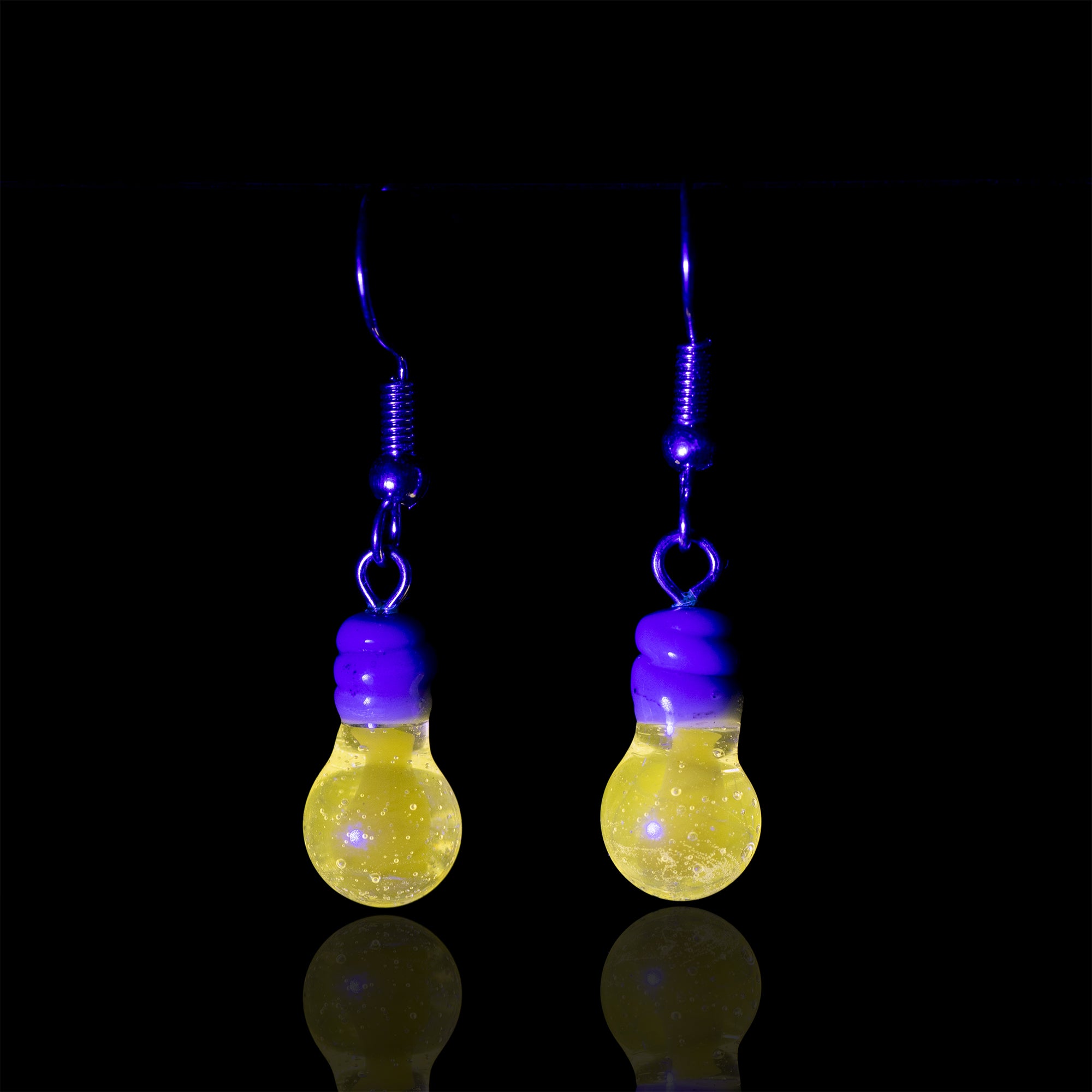 A pair of mmMelty light bulb earrings under UV light showcasing the glow of the light bulb.  