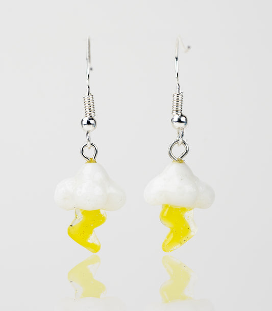 A pair of lightning cloud shaped dnagle earrings each featuring a white, fluffy cloud and a yellow lightning bolt coming from the bottom of the cloud.