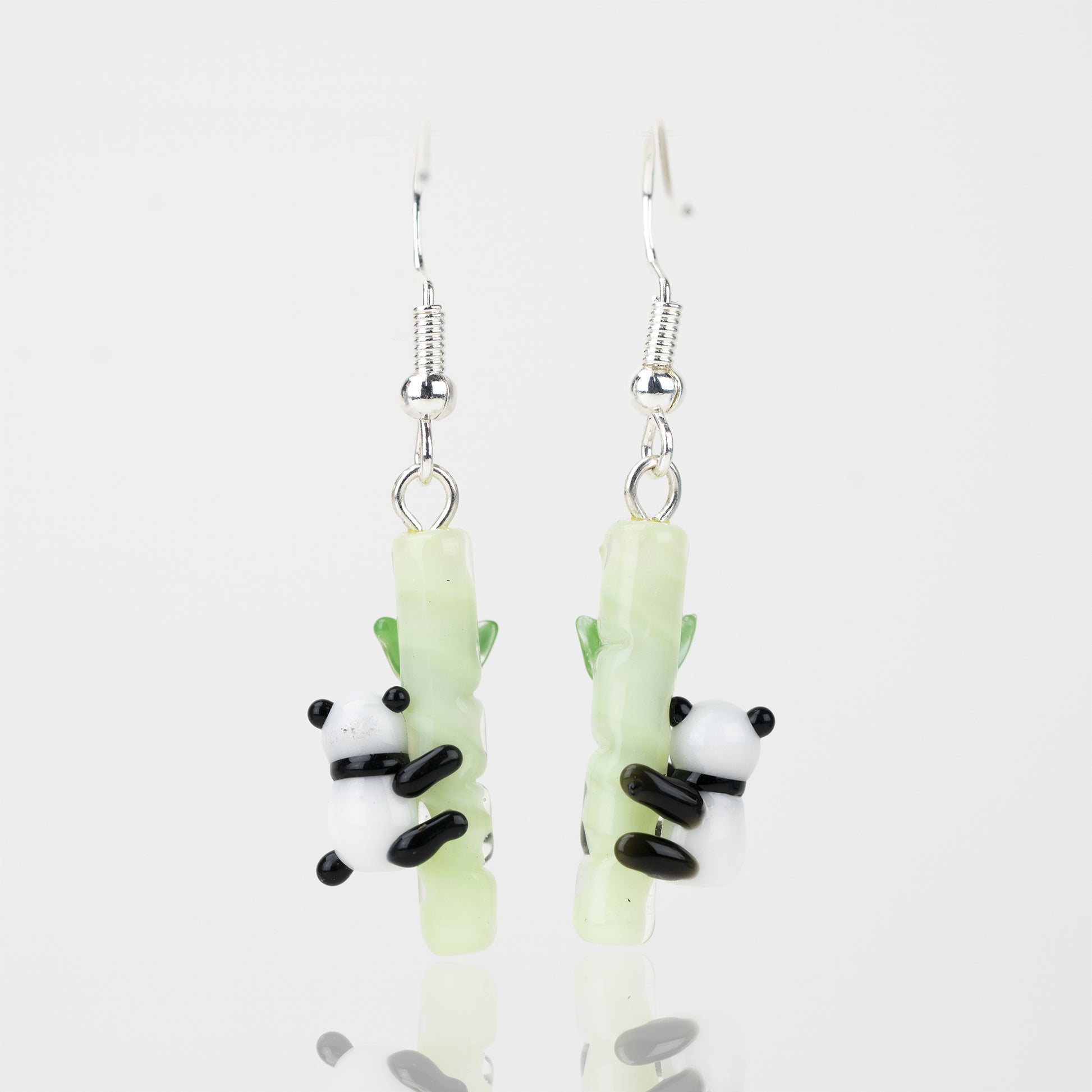 A set of two glass panda themed dangle earrings facing the back. Each earring features a black and white panda, attached to a light-green bamboo shoot. Attached to the top of the bamboo pole is a sterling silver earring hook. 