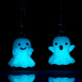A pair of two ghost shaped earring under dark-light glowing in the dark