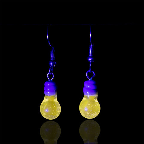 A pair of Mmelty light bulb earrings under UV light showcasing the glow of the light bulb.  