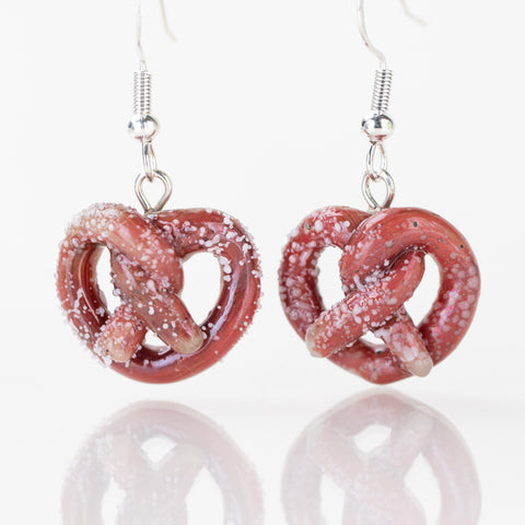 Pair of golden glass pretzel earrings on white background