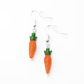 Two carrot earrings lying flat on a white table. Each earring has one carrot design with orange and green colors and a sterling silver earring hook.